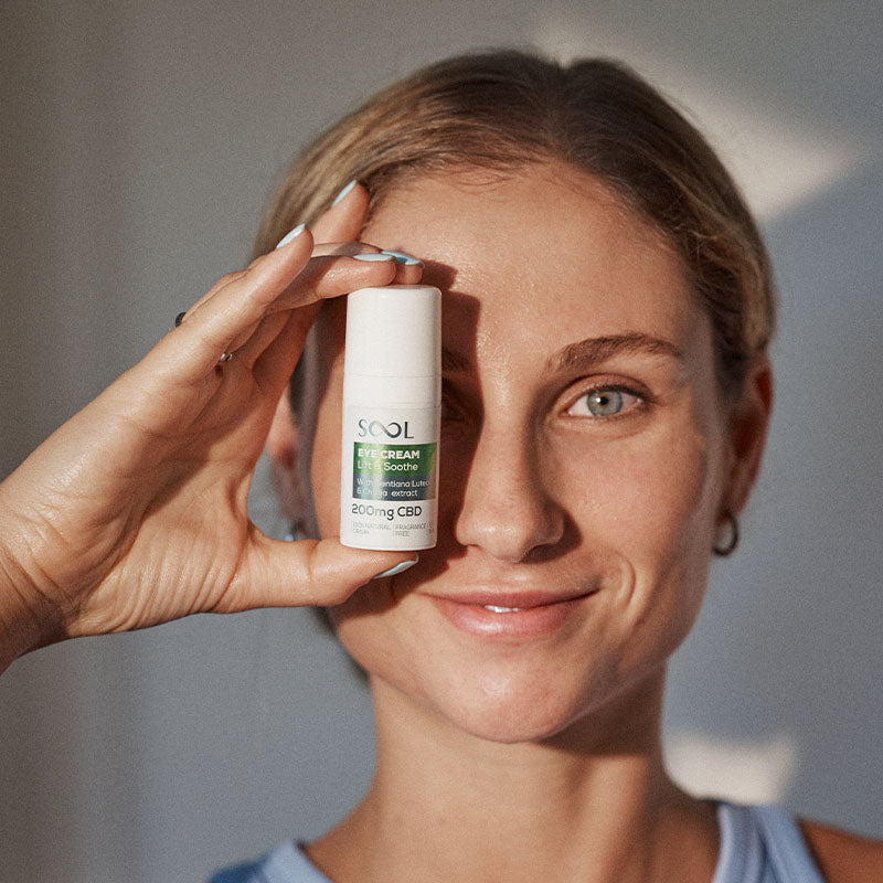 Woman holding a skincare product near her eye with a neutral background